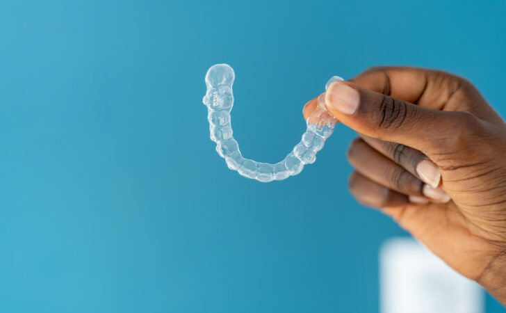 photo of clear aligner being held in front of a blue background