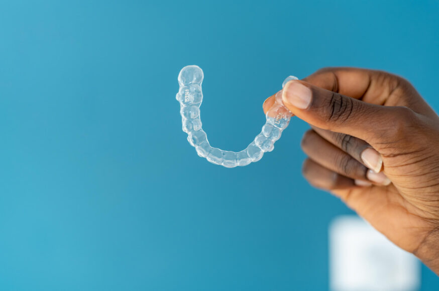photo of clear aligner being held in front of a blue background