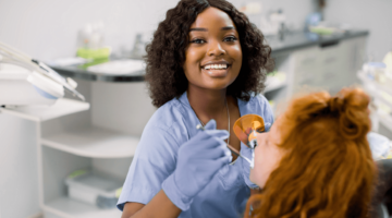 Dental assistant week: dental assistant smiling at the camera while checking on the teeth of a patient seated in the dental chair