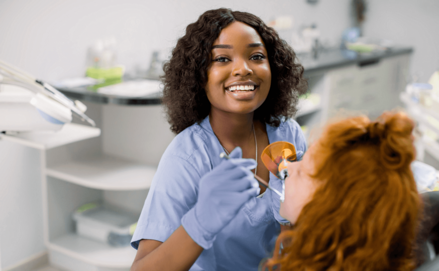 Dental assistant week: dental assistant smiling at the camera while checking on the teeth of a patient seated in the dental chair