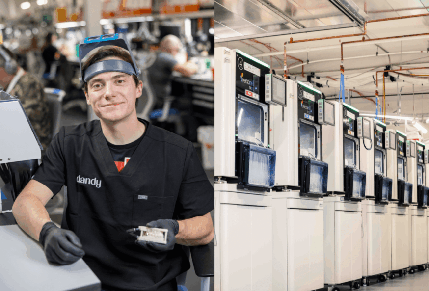 Dandy dental lab technician holding a crown beside a row of dental milling machines in the lab
